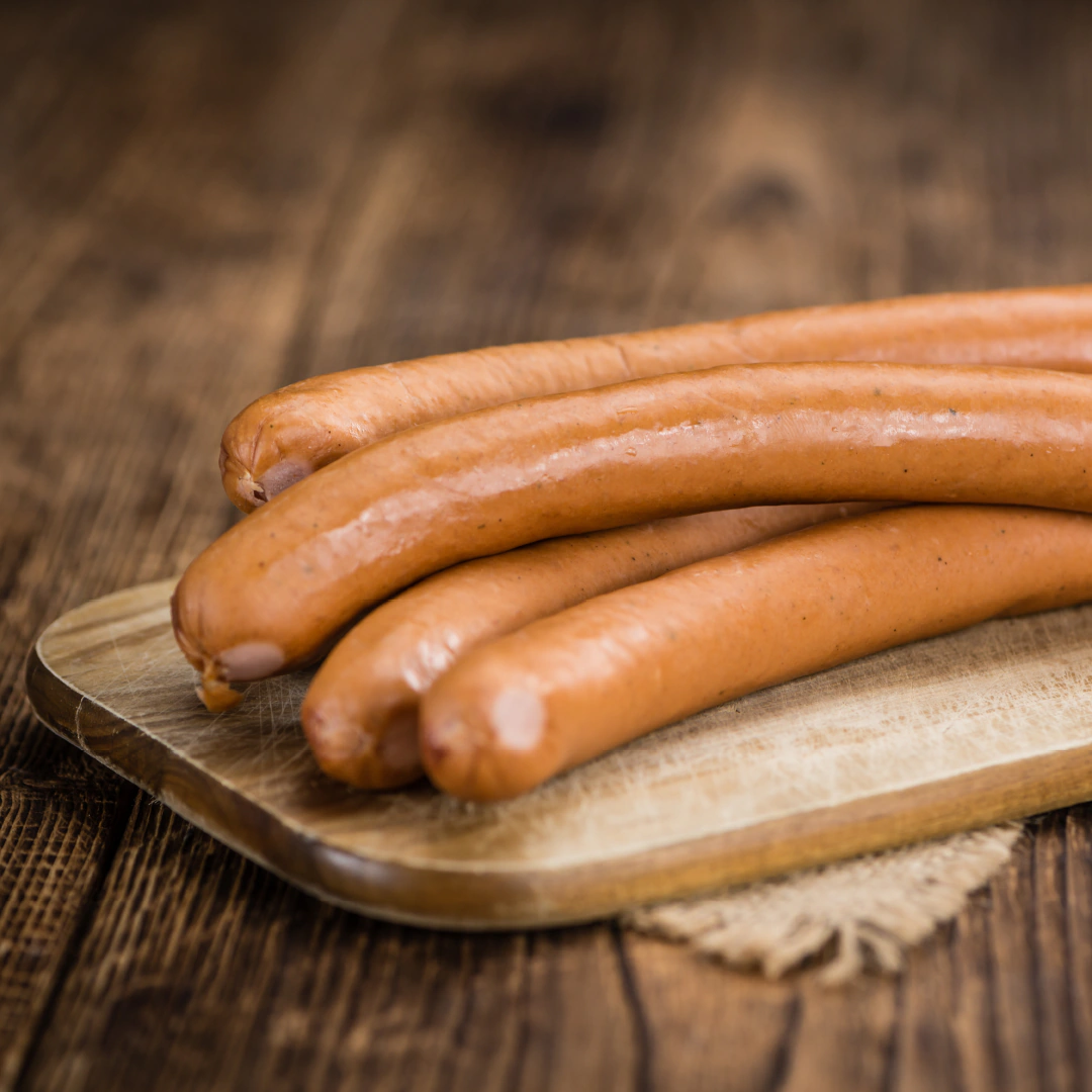Vier goldbraune Wiener Würstchen auf einem Holzbrett, angerichtet auf rustikalem Holztisch.